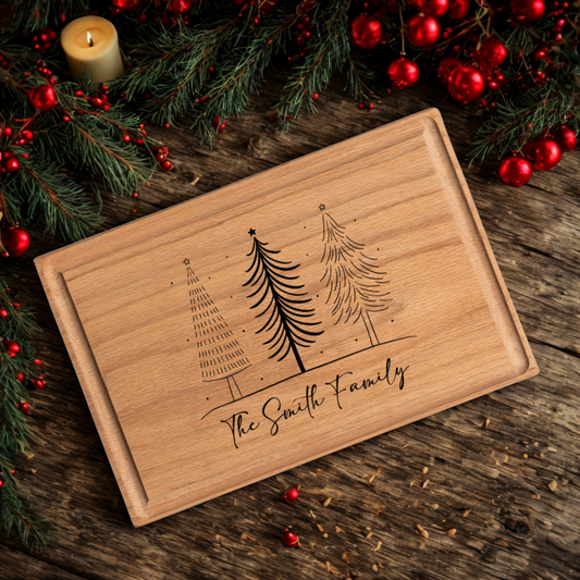 A custom cutting board engraved with three hand-drawn Christmas trees and “The Smith Family” in elegant script. The board rests on a dark wood table decorated with evergreen branches, red berries, ornaments, and a glowing candle. This festive design blends function and charm, making it an ideal personalized cutting board gift for Christmas gatherings and holiday kitchens.