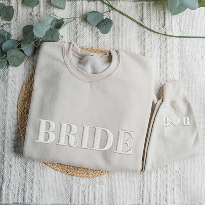Gray sweatshirt with 'BRIDE' text and matching beanie on a textured surface with eucalyptus leaves.