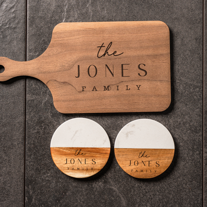 Wooden cutting board and coasters with 'the JONES FAMILY' engraving on a dark surface