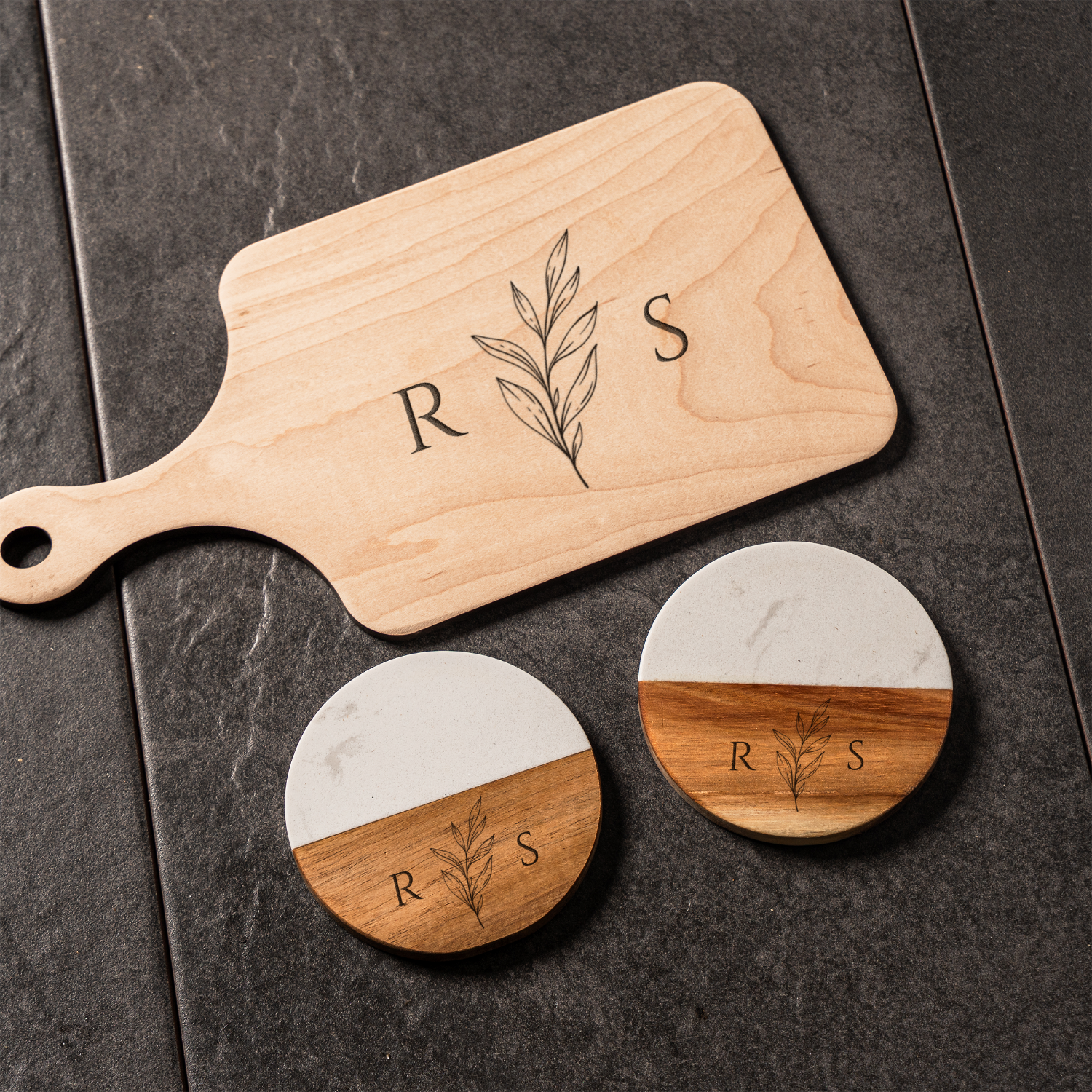Wooden cutting board with 'R S' monogram and two round coasters with the same design on a dark surface.